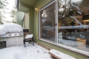 A covered outdoor area with a grill and a chair, a sliding glass door, and snow on the ground. - 2+loft | Walk to Creekside Gondola | Pet friendly (Whistler)