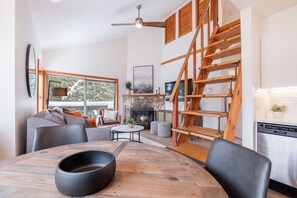 A modern living room with a fireplace, wooden staircase, and a dining area with a large table. - 2+loft | Walk to Creekside Gondola | Pet friendly (Whistler)