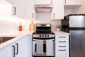 A modern kitchen with white cabinets, a stainless steel refrigerator, a black stove, and a wooden cutting board. - 2+loft | Walk to Creekside Gondola | Pet friendly (Whistler)