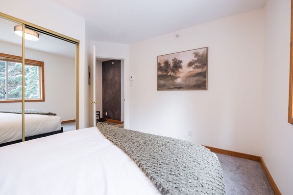 A bedroom with a bed, a window, a door, a painting, and a carpeted floor. - 2+loft | Walk to Creekside Gondola | Pet friendly (Whistler)