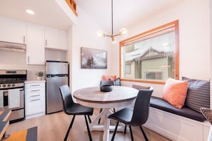A compact kitchen with modern appliances, a dining area with a round table, and a large window with a view of a house. - 2+loft | Walk to Creekside Gondola | Pet friendly (Whistler)