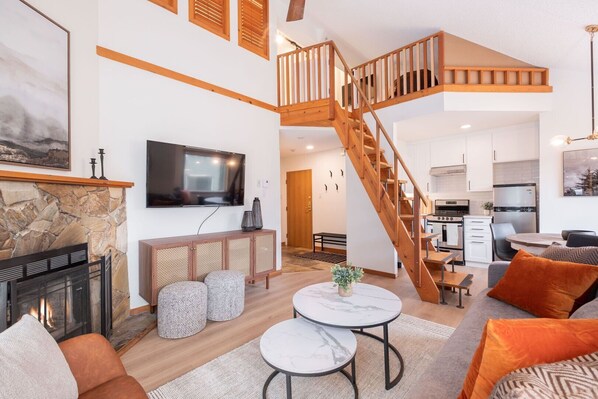 A spacious living area with a fireplace, a television, and a kitchen in the background. - 2+loft | Walk to Creekside Gondola | Pet friendly (Whistler)