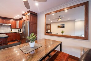 Eine moderne Küche mit Holzausbau, einem Edelstahlkühlschrank, einem Esstisch mit Pflanze und einem großen Spiegel, der den Raum widergibt.