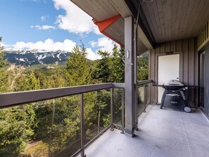 Un balcon donnant sur un paysage montagneux, un barbecue et une porte menant à l’intérieur.