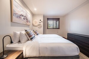 Une chambre à coucher comprenant un lit, une table de chevet, une lampe, une commode, une fenêtre et des éléments de décoration murale.