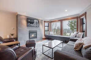 A modern living room with a fireplace, a large window with a view, and a comfortable seating area. - Spacious | Pet friendly | Shared Hot Tub | BBQ (Whistler)