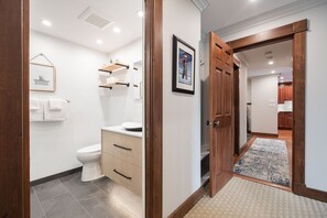 Een moderne badkamer met toilet, wastafel en opbergkasten, verbonden met een hal die uitkomt op een keuken.