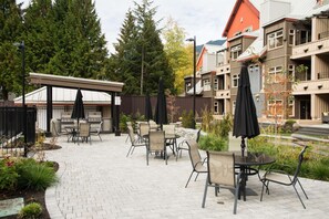 An outdoor patio with brick flooring, outdoor seating, and a grill area. - Luxury home | Creekside Gondola | Pool & hot tub (Whistler)