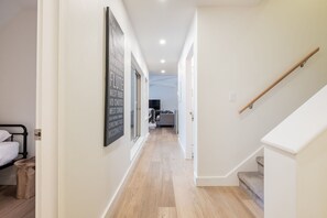 Ein Flur mit Holzboden, einer Treppe und einem Bett mit schwarzem Metallgestell.