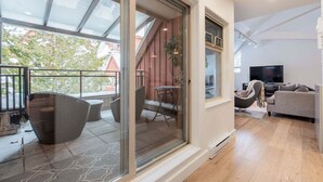 Un salon moderne doté d’une grande porte-fenêtre coulissante donnant sur un balcon, d’un canapé, d’une télévision et d’une petite table avec des chaises.
