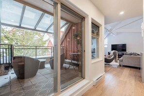 A modern living room with a large sliding glass door leading to a balcony, a sofa, a television, and a small table with chairs. - Luxury home | Creekside Gondola | Pool & hot tub (Whistler)