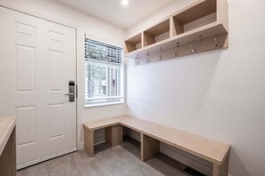A room with a white door, a window with blinds, a bench, and a wall-mounted coat rack. - Luxury home | Creekside Gondola | Pool & hot tub (Whistler)