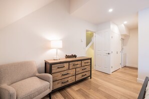 A room with a sofa, a wooden dresser, a lamp, and a staircase leading to a door. - Luxury home | Creekside Gondola | Pool & hot tub (Whistler)
