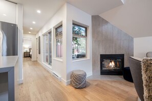 A modern living room with a fireplace, large windows, and a cozy seating area. - Luxury home | Creekside Gondola | Pool & hot tub (Whistler)