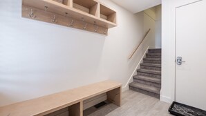 Un couloir avec un banc en bois, un porte-manteau et un escalier menant à une porte dotée d’un système de verrouillage à clavier.