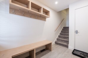 A hallway with a wooden bench, a coat rack, and a staircase leading to a door with a keypad lock. - Luxury home | Creekside Gondola | Pool & hot tub (Whistler)