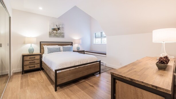 Une chambre à coucher avec un lit en bois, des tables de chevet, un banc, une fenêtre et un luminaire au plafond.