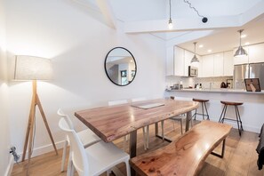 A modern kitchen with white cabinets, a wooden dining table, and bar stools. - Luxury home | Creekside Gondola | Pool & hot tub (Whistler)
