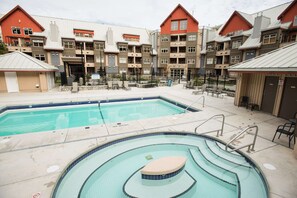 A swimming pool area with a hot tub, lounge chairs, and a view of multi-story buildings with red roofs. - Luxury home | Creekside Gondola | Pool & hot tub (Whistler)