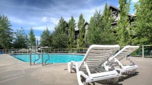 A swimming pool with white lounge chairs and a metal pool ladder. - Heated pool, hot tub & gym | Ski-in/out Retreat (Whistler)