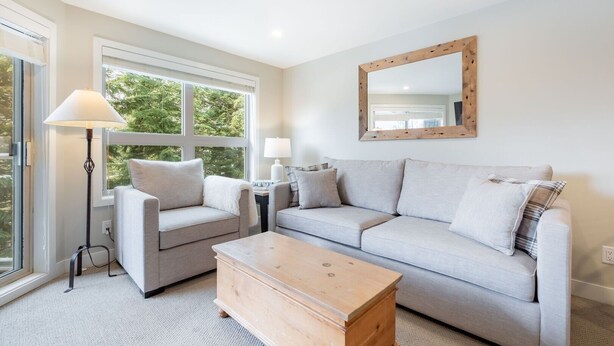 A living room with a sofa, two armchairs, a coffee table, a floor lamp, and a mirror on the wall. - Heated pool, hot tub & gym | Ski-in/out Retreat (Whistler)