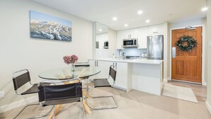 A modern kitchen with white cabinets, stainless steel appliances, and a glass dining table with two chairs. - Heated pool, hot tub & gym | Ski-in/out Retreat (Whistler)