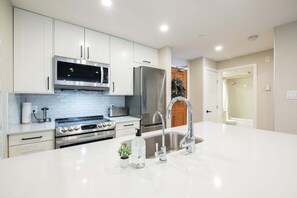 A modern kitchen with white cabinets, stainless steel appliances, a large island with a sink, and a walk-in shower. - Heated pool, hot tub & gym | Ski-in/out Retreat (Whistler)