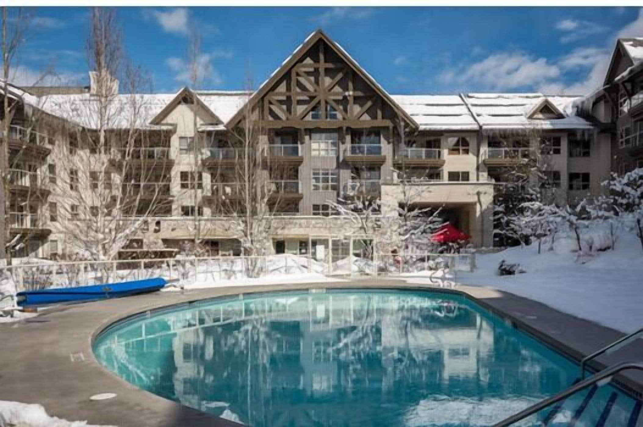 A resort with a pool, snow-covered grounds, and a multi-story building with a distinctive wooden facade.
