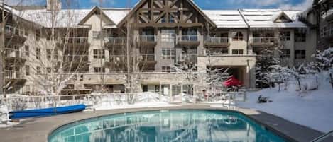 A resort with a pool, snow-covered grounds, and a multi-story building with a distinctive wooden facade.