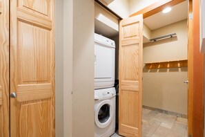 A laundry room with a washing machine and dryer, wooden doors, and a tiled floor. - BBQ | Private garage | Walk to Golfing & Lost Lake (Whistler)