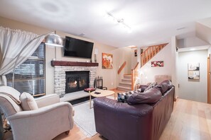 A living room with a fireplace, a sofa, a TV, and a staircase. - BBQ | Private garage | Walk to Golfing & Lost Lake (Whistler)