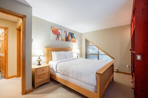 Une chambre à coucher avec un lit en bois, deux tables de chevet avec des lampes, une grande fenêtre avec des stores et un tableau abstrait aux couleurs vives accroché au mur.