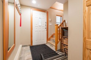 Un couloir avec un escalier en bois, une porte blanche et un paillasson noir à l’entrée.