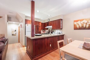 A modern kitchen with wooden cabinets, a central island, and a dining area with a table and chairs. - BBQ | Private garage | Walk to Golfing & Lost Lake (Whistler)