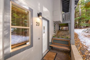 A building entrance with a number 20 sign, a bench, and a small garden area with a wooden bench and a metal railing. - BBQ | Private garage | Walk to Golfing & Lost Lake (Whistler)