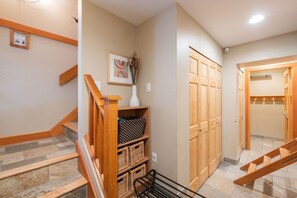 A hallway with a wooden staircase, a white vase with a plant, and a framed picture on the wall. - BBQ | Private garage | Walk to Golfing & Lost Lake (Whistler)
