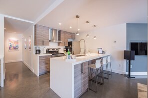 Una cocina moderna con una isla central, taburetes de bar, iluminación colgante y electrodomésticos de acero inoxidable.