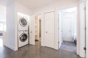 A laundry area with stacked washers and dryers, a hallway with white doors, and a carpeted bedroom. - Gorgeous townhouse | Private hot tub | BBQ (Whistler)