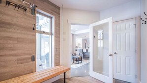 A modern interior with a wooden bench, a white door, and a view into a kitchen area. - Gorgeous townhouse | Private hot tub | BBQ (Whistler)