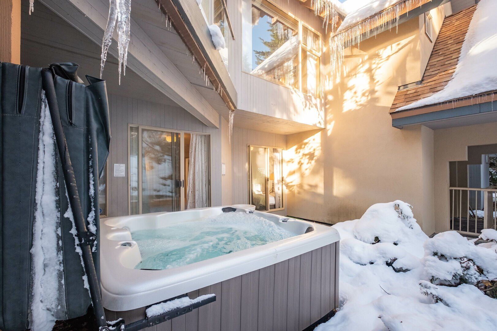 Ein Whirlpool in einer verschneiten Außenanlage mit einer Holzterrasse und einer Glastür, die zu einem Raum führt.