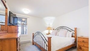 A bedroom with a wooden bed, a nightstand, a dresser, and a television on a stand. - Gorgeous townhouse | Private hot tub | BBQ (Whistler)