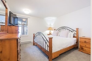 A bedroom with a wooden bed, a nightstand, a dresser, and a television on a stand. - Gorgeous townhouse | Private hot tub | BBQ (Whistler)