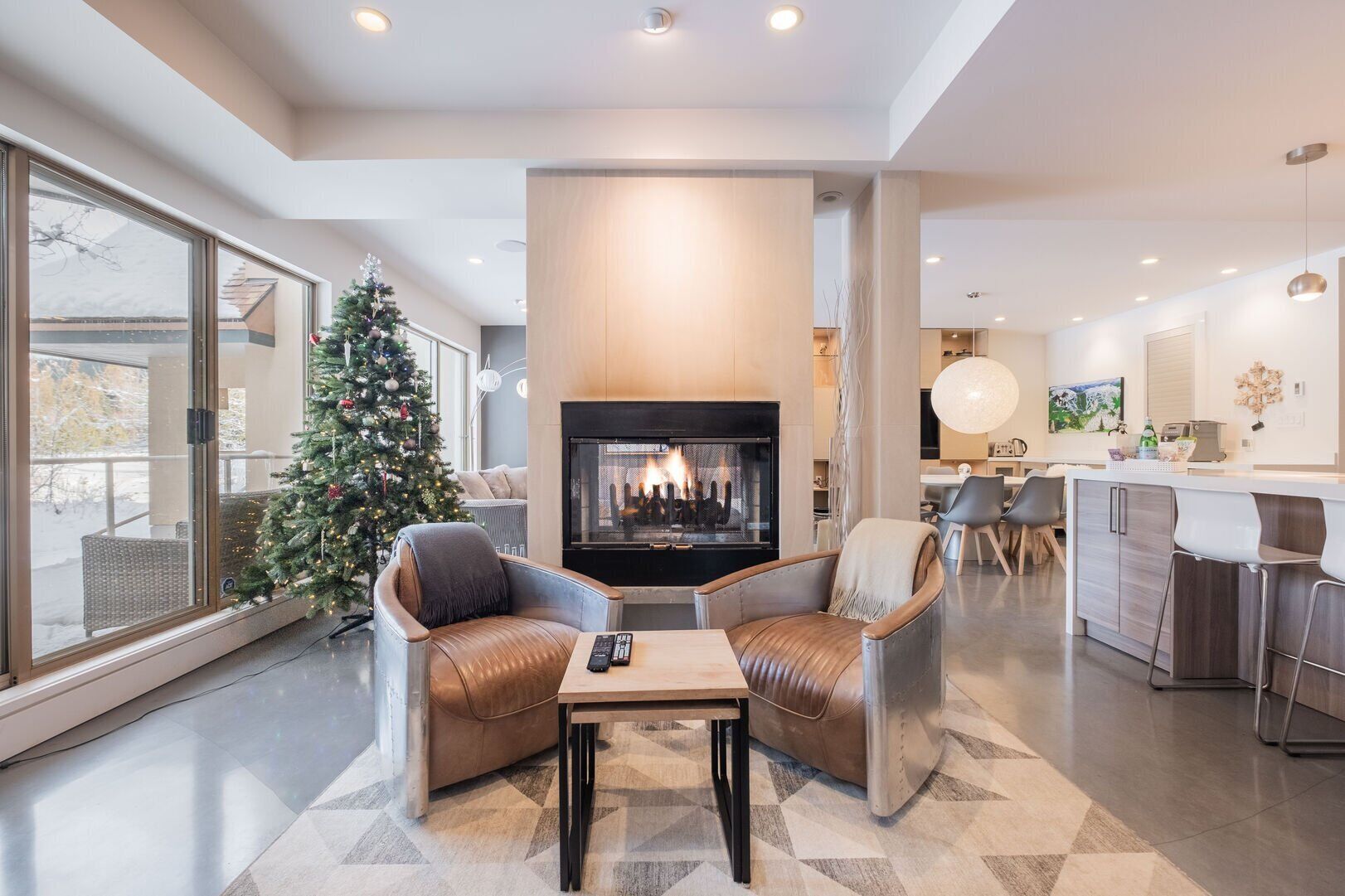 Ein modernes Wohnzimmer mit Kamin, Ledersesseln, einem Couchtisch und einem Weihnachtsbaum.