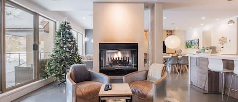 Ein modernes Wohnzimmer mit Kamin, Ledersesseln, einem Couchtisch und einem Weihnachtsbaum.
