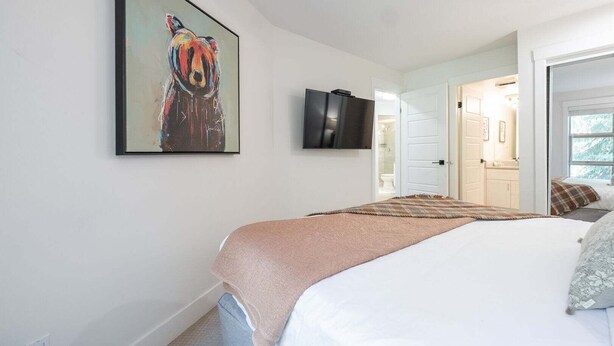 A bedroom with a bed, a television, a door leading to a bathroom, and a painting on the wall. - Luxury ski-in/out | Complex pool, hot tub & gym | BBQ (Whistler)