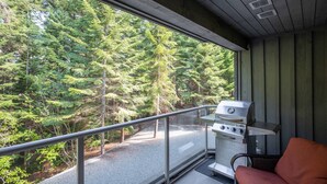A balcony with a grill, a chair, and a view of a forest. - Luxury ski-in/out | Complex pool, hot tub & gym | BBQ (Whistler)