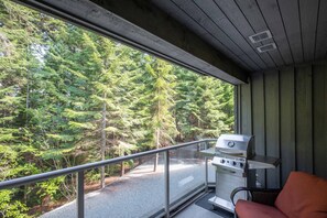 Ein Balkon mit Grill, Stuhl und Blick auf einen Wald.