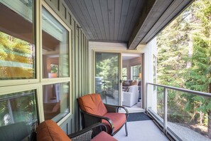 A balcony with a view of a forest, a chair, and a sofa. - Luxury ski-in/out | Complex pool, hot tub & gym | BBQ (Whistler)