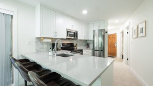 A modern kitchen with white cabinets, stainless steel appliances, and a large island with bar stools. - Luxury ski-in/out | Complex pool, hot tub & gym | BBQ (Whistler)