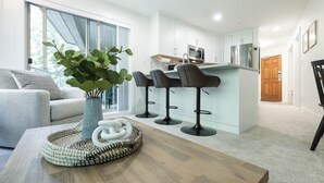 A modern kitchen with white cabinets, a stainless steel refrigerator, and a bar area with two stools. - Luxury ski-in/out | Complex pool, hot tub & gym | BBQ (Whistler)
